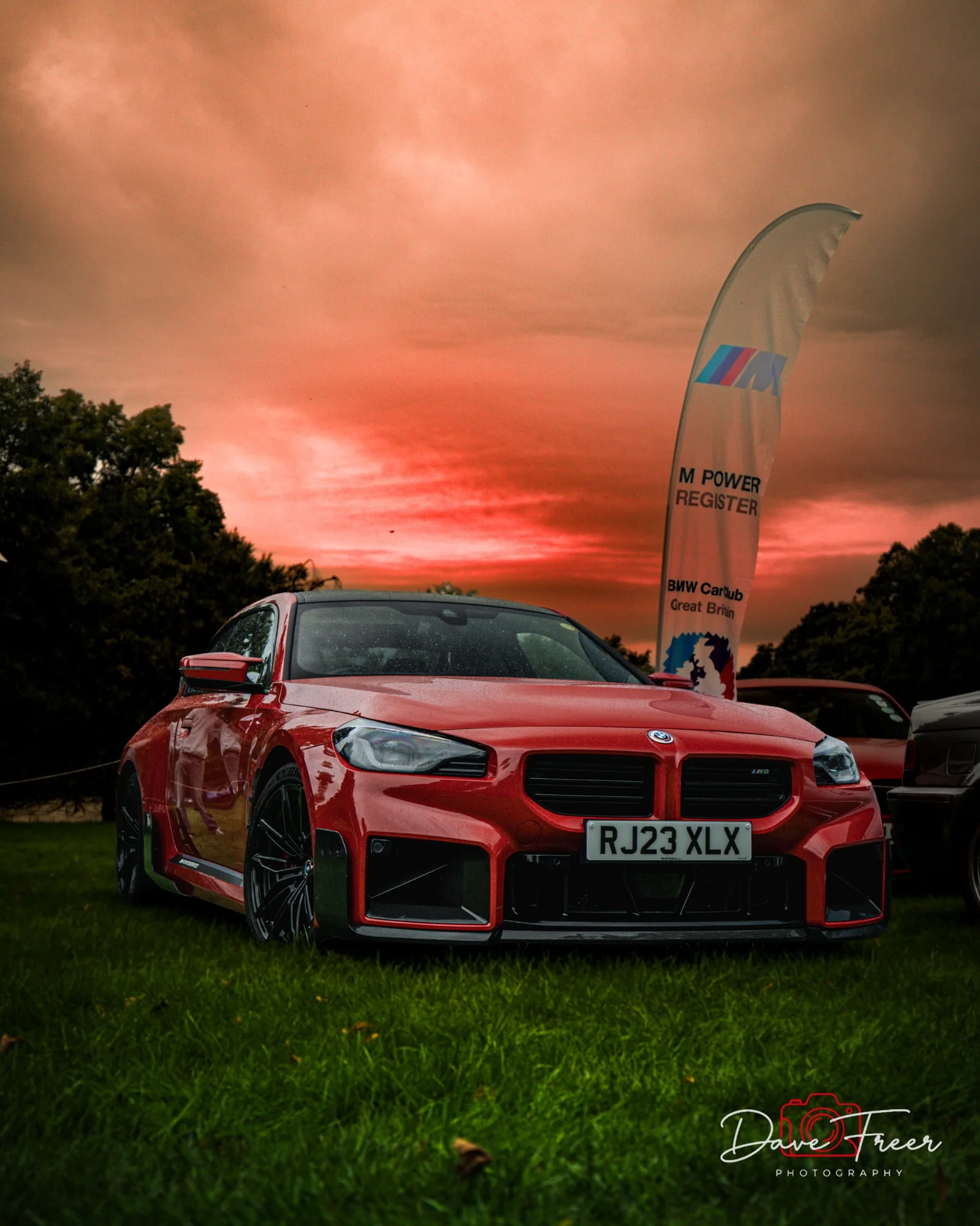 Red BMW at an outdoor car event beneath a vivid sky